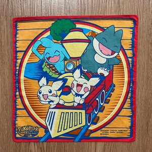 May include: A colorful Pokemon The Park 2005 bandana featuring a train with Pikachu, a blue Pokemon, and a gray Pokemon. The train is on a track with a wooden background.