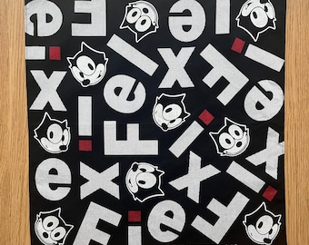 Może przedstawiać: Czarna kwadratowa bandana z powtarzającym się wzorem słowa "Felix" w kolorze białym oraz kreskówkowymi obrazkami Kota Felixa. Czerwone kwadraty akcentują wzór. Tekst "©1990 FELIX THE CAT PRODUCTIONS, INC" jest wydrukowany na dole.