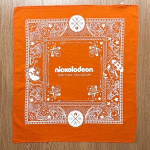 Peut inclure: Bandana orange avec un motif cachemire et dessins animés blancs. Le centre présente le logo Nickelodeon Writing Program. Le bandana est de forme carrée et en tissu. Le motif comprend des crânes, des crayons et des étoiles.