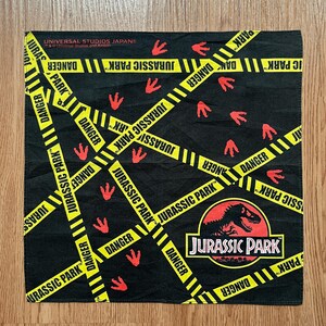 May include: Black Jurassic Park bandana with yellow hazard stripes and red dinosaur footprints. The bandana features the Jurassic Park logo and the text "DANGER".