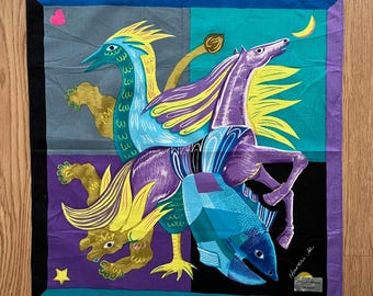 May include: A colorful square scarf with a design of a purple horse, a blue fish, a yellow lion, and a blue bird. The scarf has a black border and a white signature in the bottom right corner.
