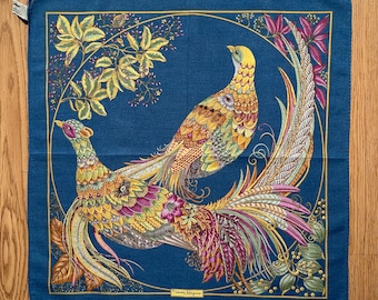 May include: A blue silk scarf with a colorful design of two peacocks with intricate patterns and a floral border. The scarf features the text "Salvatore Ferragamo" in gold lettering.