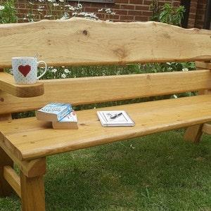 May include: A wooden bench with a natural finish and a heart-shaped mug on the armrest. The bench is made of solid wood and has a rustic look. There are two books on the seat of the bench.