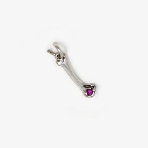 May include: A silver bone-shaped pendant with a small, round, magenta stone set near the base. The pendant has a loop at the top for a chain. The jewellery is set against a white background.