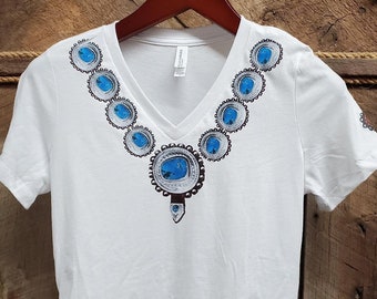 May include: White t-shirt with a blue and silver turquoise necklace design. The necklace design is on the front of the shirt and the bottom hem.