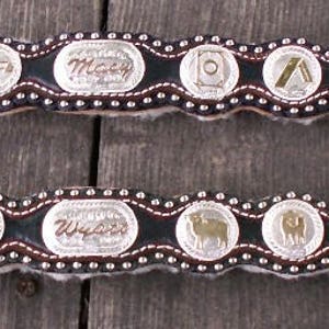 Puede incluir: Dos cinturones de cuero marr&oacute;n con hebillas plateadas y medallones plateados decorativos. Los medallones tienen varios dise&ntilde;os, incluyendo animales y patrones geom&eacute;tricos.