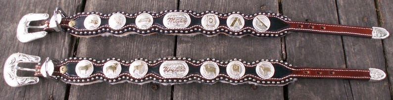 Puede incluir: Dos cinturones de cuero marr&oacute;n con hebillas plateadas y medallones plateados decorativos. Los medallones tienen varios dise&ntilde;os, incluyendo animales y patrones geom&eacute;tricos.
