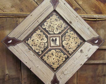 May include: A square wooden frame with a diamond-shaped leather inlay. The leather is intricately carved with floral patterns and has a dark brown color. The frame is painted a light brown color and has a distressed look.