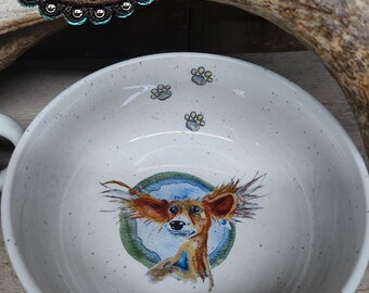 May include: White ceramic dog bowl with a brown and white dog illustration and paw prints. The bowl has a speckled glaze.