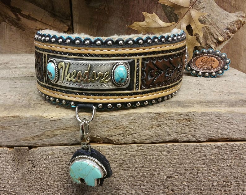 Puede incluir: Un collar de perro de cuero marr&oacute;n con una placa de nombre plateada que dice "Theodore". El collar est&aacute; decorado con piedras turquesa y tachuelas plateadas. Un amuleto plateado a juego con una piedra turquesa est&aacute; unido al collar.