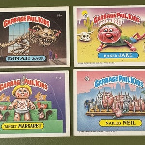 May include: Four vintage Garbage Pail Kids trading cards. The cards feature grotesque cartoon characters with humorous names like "Dinah Saur", "Baked Jake", "Target Margaret", and "Nailed Neil". The cards have a white border and colourful backgrounds.