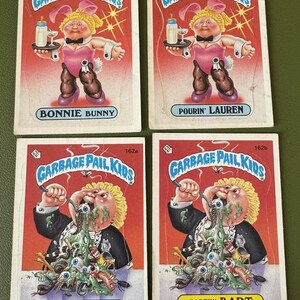 May include: Four Garbage Pail Kids trading cards. The cards feature illustrations of different characters. The first card shows a girl in a pink bunny costume holding a tray with a bottle and a glass. The second card shows a girl in a pink bunny costume holding a tray with a bottle and a glass. The third card shows a boy with green goo dripping from his mouth. The fourth card shows a boy with green goo dripping from his mouth.