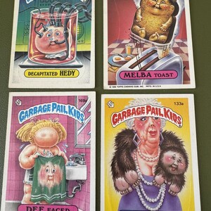 Może przedstawiać: Cztery karty kolekcjonerskie Garbage Pail Kids przedstawiające różne postacie. Karty są żółte, różowe i niebieskie z białymi obramowaniami. Postacie to Decapitated Hedy, Melba Toast, Dee Faced i Furry Murray. Karty pochodzą z 1986 Topps Chewing Gum, Inc.