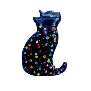 May include: A black cat ornament featuring a starry night design. The cat is decorated with colourful, sparkling gems and star-shaped accents. The cat is in a sitting position with its head tilted upwards.