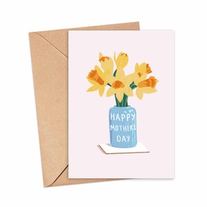May include: A greeting card with a pink background featuring a blue vase with yellow daffodils. The vase has the text "Happy Mother's Day" written on it.