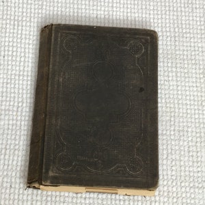 May include: A dark brown leather-bound book with an intricate embossed design on the cover. The design features a central clover shape surrounded by a decorative border.