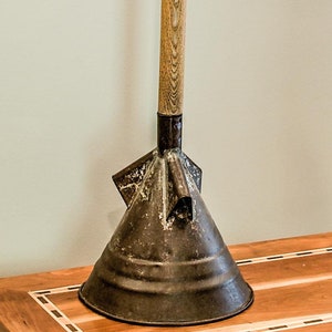 Op de afbeelding: Een vintage metalen trechter met een houten handvat. De trechter is donkergrijs en heeft een brede, uitlopende opening. Het handvat is bruin en heeft een natuurlijke houtnerf.