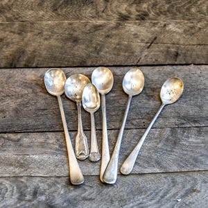May include: Six silver spoons with long handles, arranged on a wooden surface.