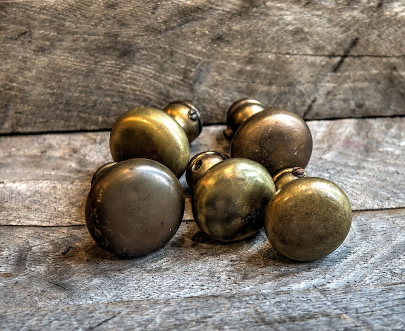 May include: Six antique brass door knobs with a worn finish. The knobs are round and have a simple design.