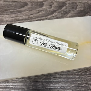 May include: A clear glass roll-on bottle with a black cap. The label reads "Love & Lotus Designs Mr. Mantic".
