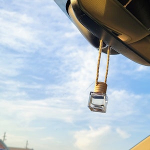 May include: A clear glass bottle with a brown cork hanging from a string inside a car. The bottle is hanging from the rearview mirror.