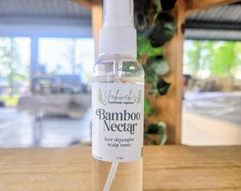 Könnte beinhalten: Eine transparente Sprühflasche mit "Yahweh's handmade organics" Bamboo Nectar Haarentwirrer und Kopfhaut-Tonic. Das weiße Etikett hat grüne Akzente und schwarzen Text. Die Flasche enthält 30 ml Produkt und steht auf einer Holzoberfläche.