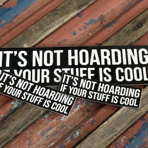 May include: Three rectangular black stickers of varying sizes, each featuring the white text "IT'S NOT HOARDING IF YOUR STUFF IS COOL" in a bold, sans-serif font. The stickers are arranged in a cluster, displaying the same phrase in three different scales.
