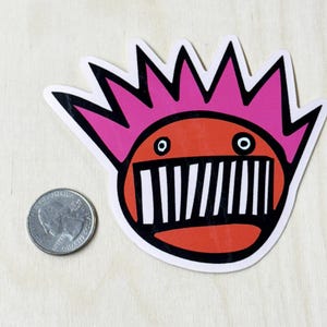 May include: A red and pink cartoon sticker with a mouth full of black and white teeth. The cartoon has a pink mohawk and large, white eyes.