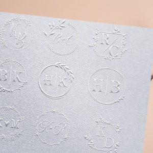 以下が含まれることがあります： 花柄のアクセントが付いた、異なる9つのモノグラムデザイン。各デザインは、円形または正方形のフレーム内に2つの文字の組み合わせを特徴としています。