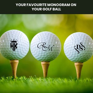 K&ouml;nnte beinhalten: Drei wei&szlig;e Golfb&auml;lle mit schwarzen personalisierten Monogrammen. Die Monogramme sind "HK" mit einer Krone &uuml;ber den Buchstaben, "R&M" in einer kursiven Schrift und "DS" mit einer dekorativen Verzierung.
