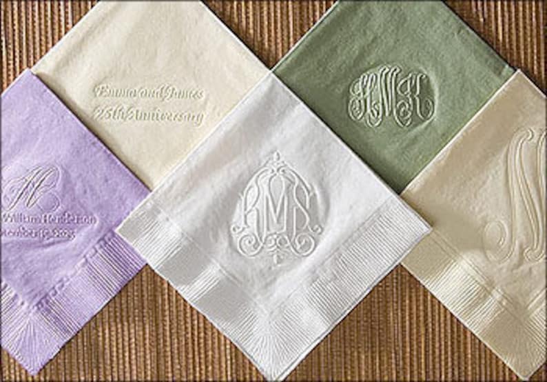 May include: Five different colors of paper napkins with embossed designs. The napkins are folded in half and have a white border. The designs include a monogram, a wedding anniversary message, and a floral design.