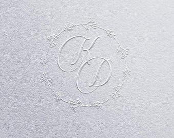 May include: A white embossed monogram with the letters "KD" surrounded by a delicate floral wreath.