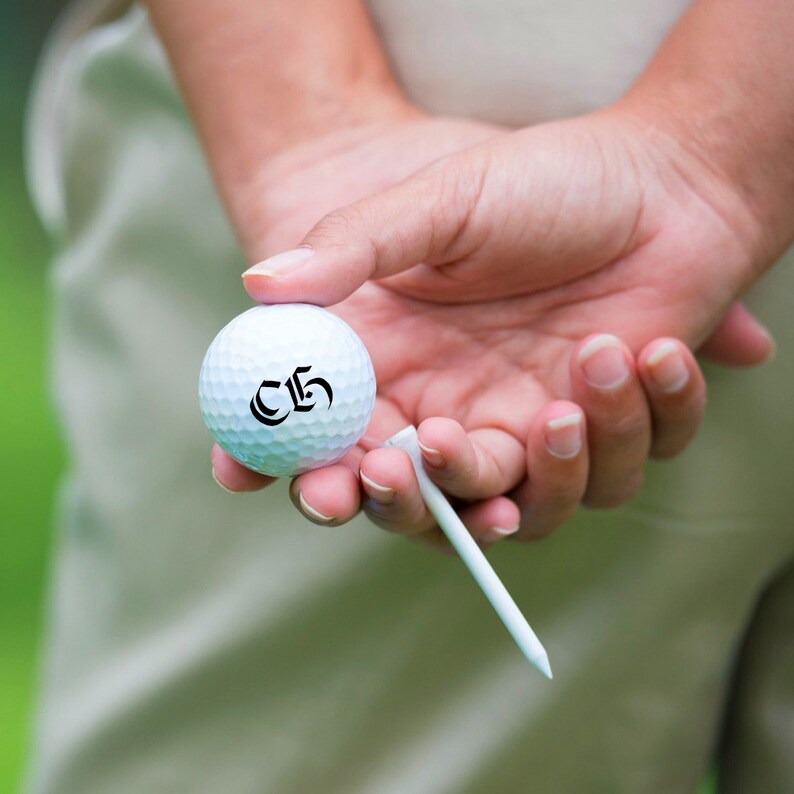 K&ouml;nnte beinhalten: Ein wei&szlig;er Golfball mit der Nummer "C5" darauf, in einer Hand mit einem Abschlagtee gehalten.