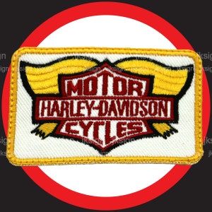 May include: A white embroidered patch with a yellow border. The patch features the Harley-Davidson logo with the words "Motor", "Harley-Davidson", and "Cycles" in red.