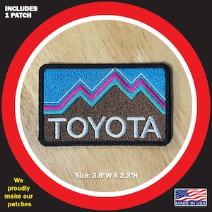 May include: Rectangular patch featuring a mountain range design with blue, pink, and brown colors. The word "TOYOTA" is embroidered in white. The patch measures 3.8"W x 2.3"H and includes the text "MADE IN USA".