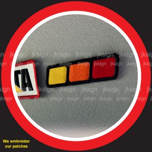 May include: Two embroidered patches. One is a red, white, and yellow patch with the word "GTA" in white letters. The other is a black, red, orange, and yellow patch with three rectangular sections.