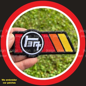 May include: Embroidered patch with a white circle containing the Japanese characters for "Toyota" in black. The circle is on a red background with orange and yellow stripes.