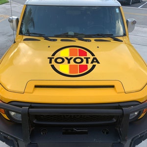 Peut inclure: Toyota FJ Cruiser jaune avec un pare-chocs avant noir et un logo Toyota noir et rouge sur le capot.