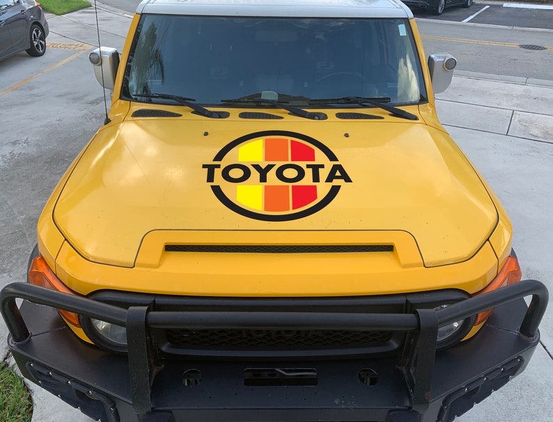 Peut inclure: Toyota FJ Cruiser jaune avec un pare-chocs avant noir et un logo Toyota noir et rouge sur le capot.