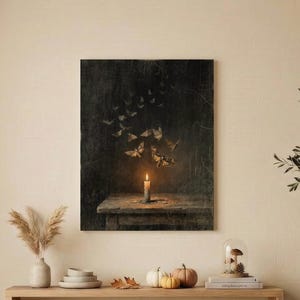 May include: A rectangular wall art print featuring a dark, moody scene of a single lit candle on a wooden table with a swarm of moths flying upward into the shadows. The artwork is displayed in a living room setting above a long wooden console table.