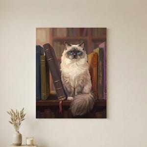 May include: A rectangular wall art print featuring a fluffy, cream-colored cat with dark brown points and bright blue eyes sitting on a wooden shelf. The cat is positioned between several upright, colorful hardcover books in a library setting.