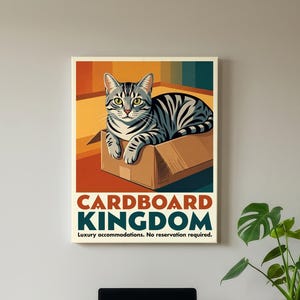 May include: A rectangular wall poster featuring a grey tabby cat sitting inside a brown cardboard box. The text reads CARDBOARD KINGDOM and Luxury accommodations. No reservation required. The background has vertical stripes in orange, yellow, and blue.