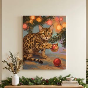May include: A square wall art print featuring a spotted Bengal cat sitting under pine branches, batting at a red Christmas ornament. The cat has golden-brown fur with dark spots. The background includes warm glowing lights and a red ornament on the floor.