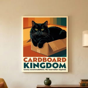 May include: A rectangular wall art print featuring a black cat sitting inside a brown cardboard box. The text reads CARDBOARD KINGDOM and Luxury accommodations. No reservation required. The background has colorful vertical stripes.