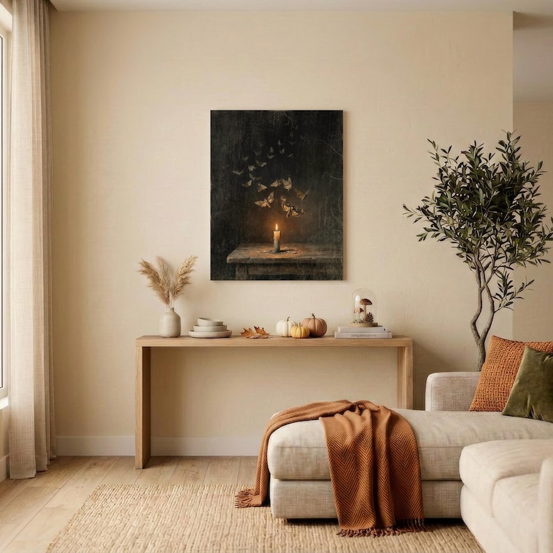 May include: A rectangular wall art print featuring a dark, moody scene of a single lit candle on a wooden table with a swarm of moths flying upward into the shadows. The artwork is displayed in a living room setting above a long wooden console table.