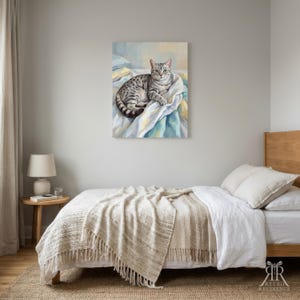 May include: A rectangular wall art print featuring a painting of a grey tabby cat with green eyes resting on white and blue rumpled fabric. The cat is positioned in the center of the canvas, which is displayed above a bed in a bedroom setting.