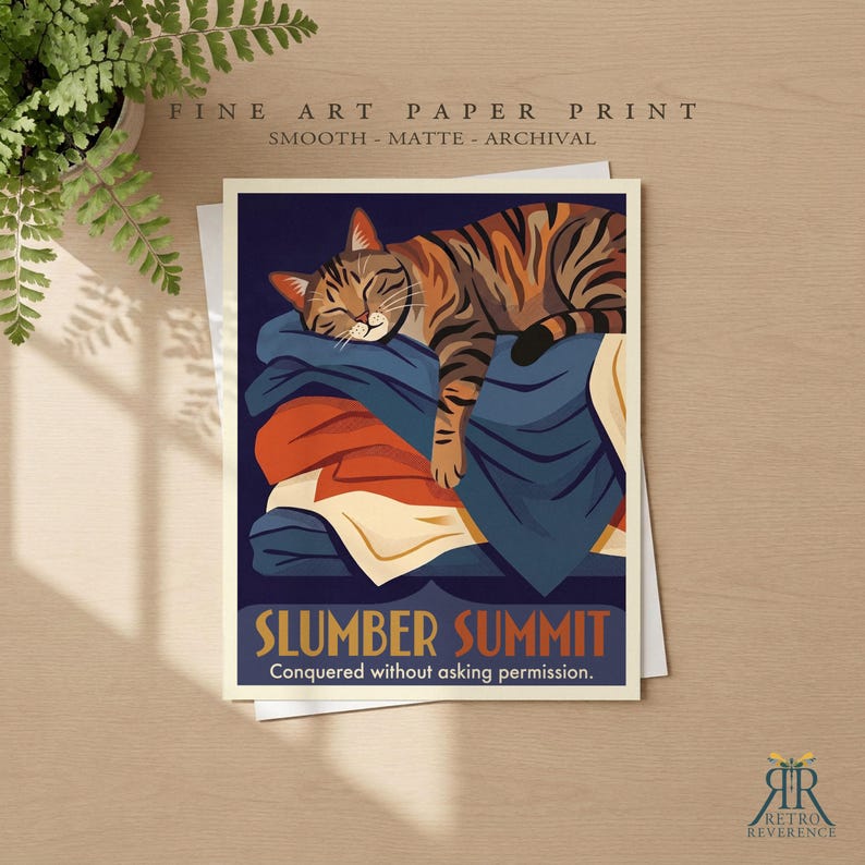 May include: A fine art paper print featuring a brown tabby cat sleeping on a stack of blue, orange, and cream-colored blankets. The text reads SLUMBER SUMMIT and Conquered without asking permission. The print is smooth, matte, and archival.