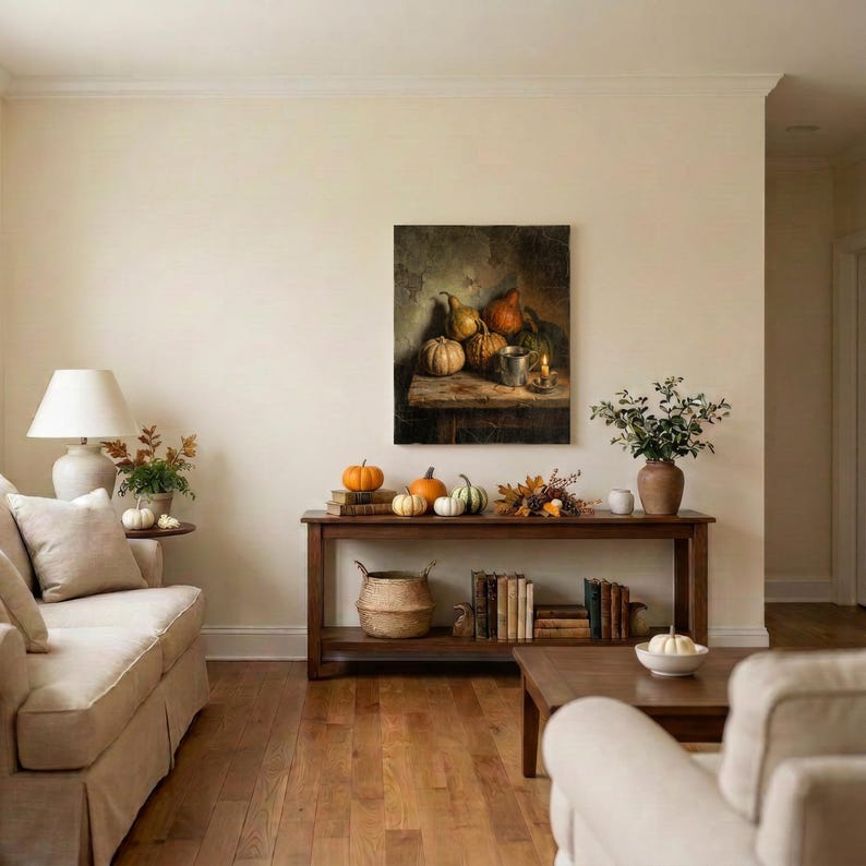 May include: A rectangular wall painting depicting a still life of pumpkins and a metal cup on a wooden table. The artwork features warm, earthy tones and is displayed above a long wooden console table holding pumpkins, books, and a plant.
