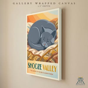 May include: A gallery wrapped canvas with a 3.8 cm depth featuring a graphic illustration of a grey cat curled up on a bed. The text reads SNOOZE VALLEY THE CENTER OF THE BED IS ALWAYS TAKEN. The background displays warm orange and yellow tones.