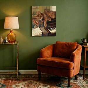 May include: A rectangular wall art print featuring a brown cat resting on a piano with sheet music and a small vase of flowers. The artwork is displayed on a solid olive green wall above a burnt orange velvet armchair in a room setting.